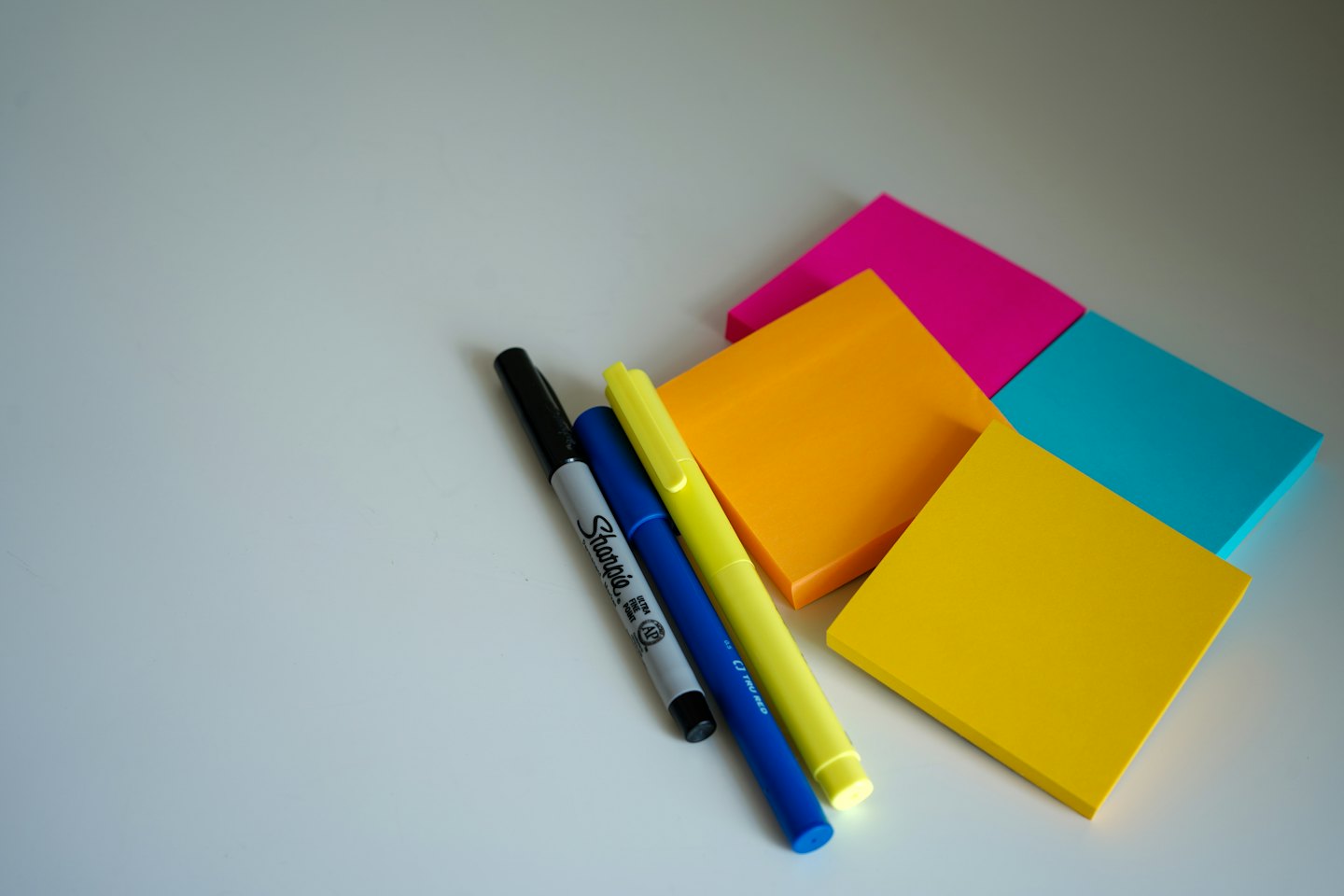 Pens and colorful sticky notes arranged on a white surface.