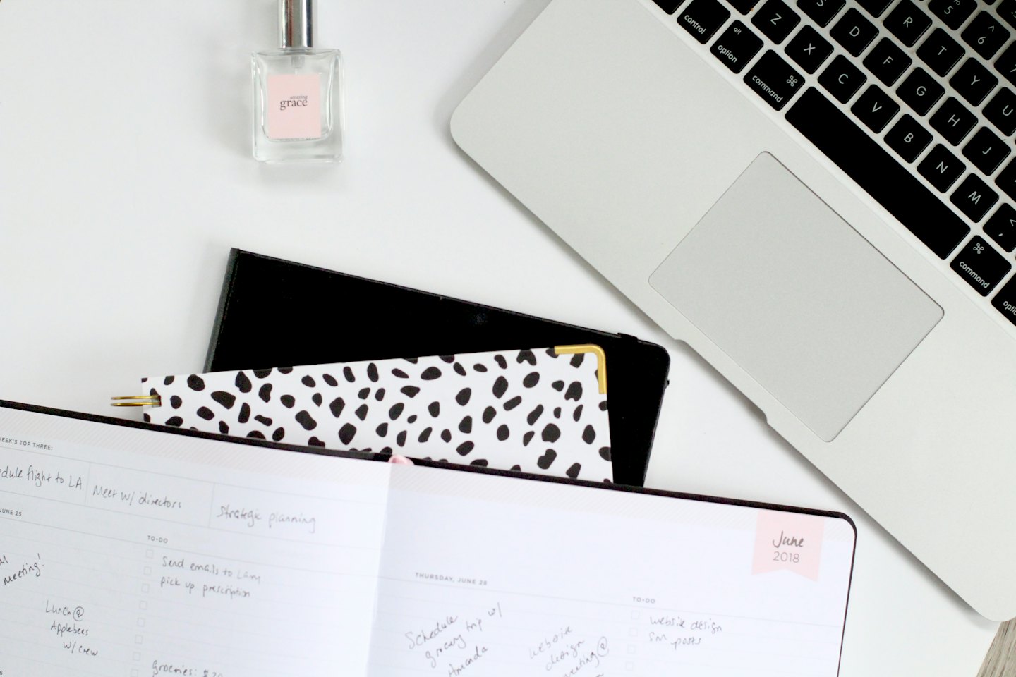 Laptop, planner, and perfume bottle arranged on a desk.